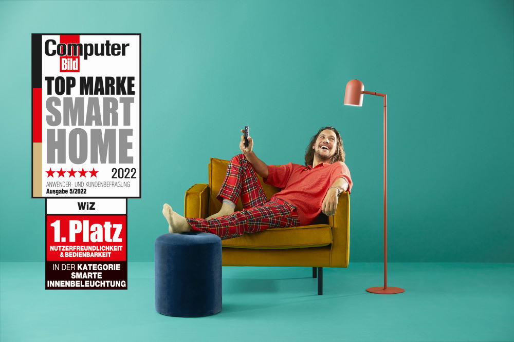 WiZ Testsieger für Smart Home 1. Platz für Kundenfreundlichkeit und Bedienbarkeit in 2022: Person sitzt in einem Sessel und lächelt in Richtung einer Stehlampe.